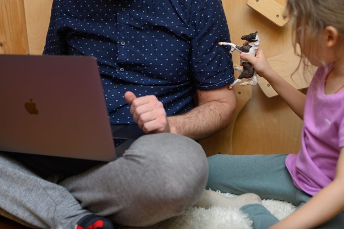 a man working from home using a laptop and his little daughter playing with childrens toys concept of t ydAwk