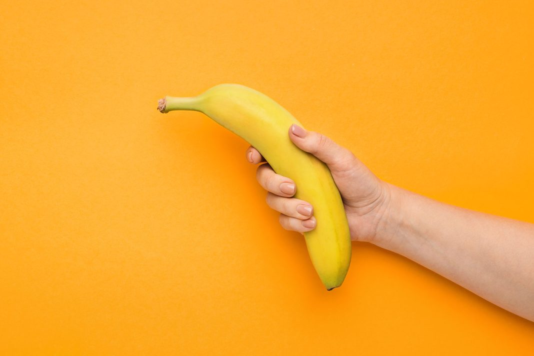 Ženska ruka koja drži bananu na narančastoj pozadini