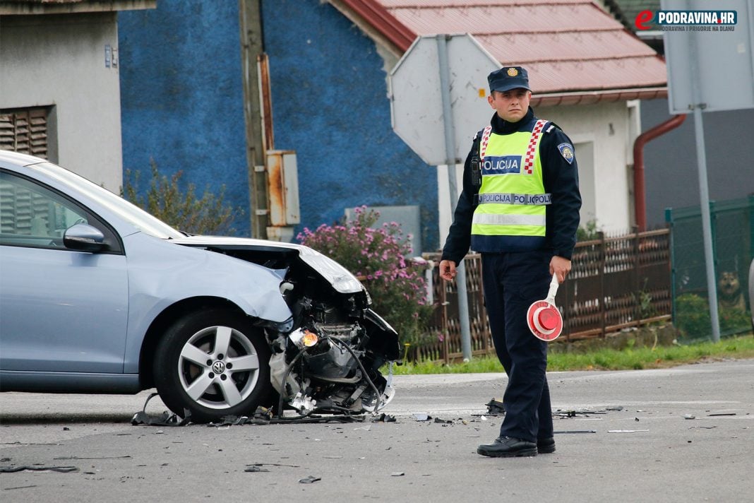 Policajac na raskrižju pokraj razbijenog automobila, prometna nezgoda